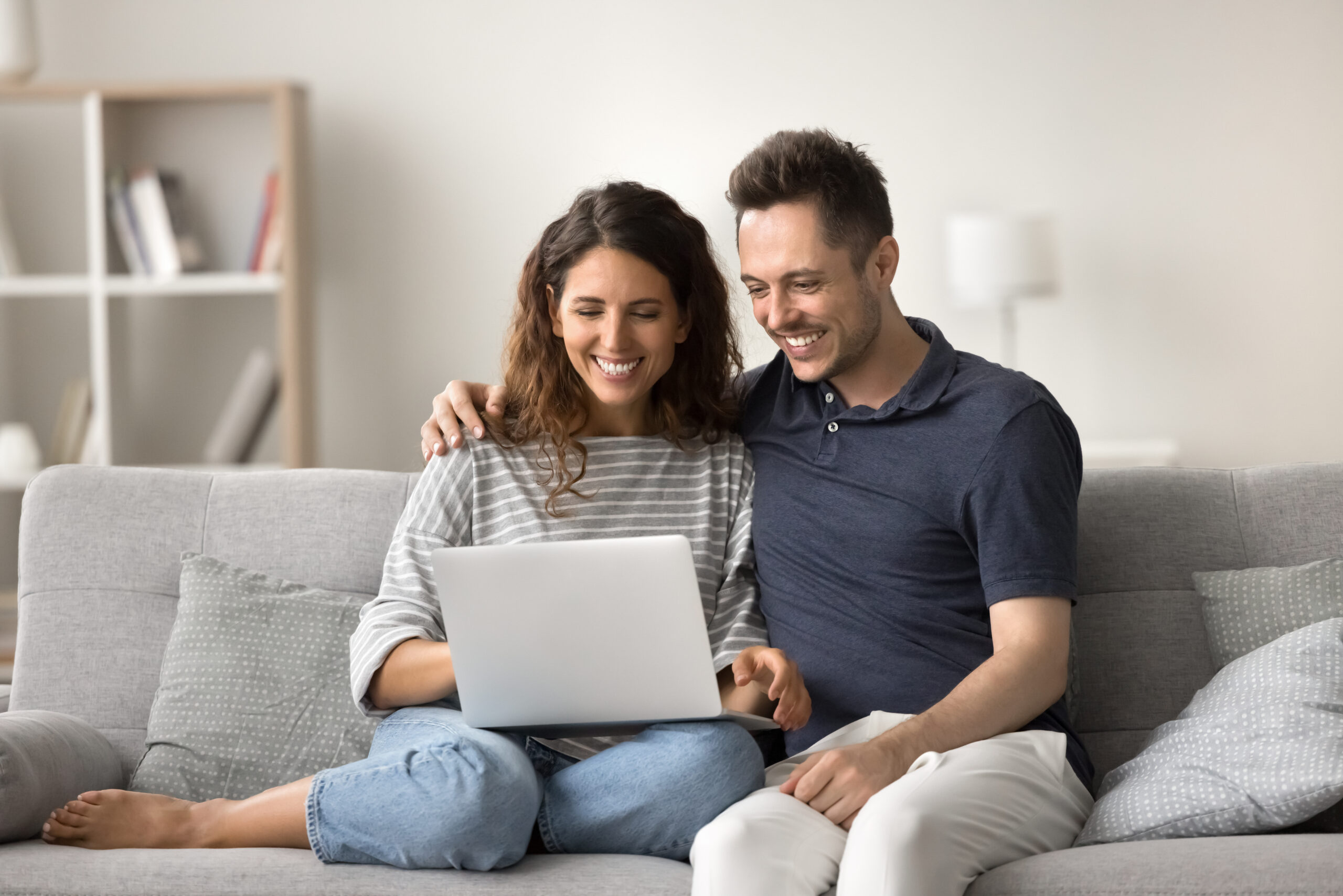 Cheerful couple using a laptop together on a sofa to book eco-friendly house cleaning services online with Enovana Green Cleaning in Raleigh NC